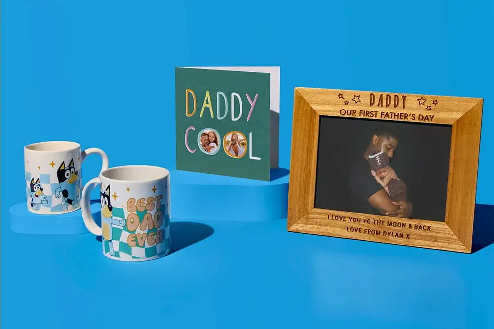 Fathers Day gift display on a blue background featuring two patterned mugs, a Daddy Cool photo card, and a personalised wooden photo frame